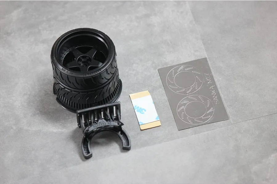Pandora RC steering wheel accessory for Sanwa transmitters, including a wheel-shaped grip, mounting bracket, adhesive strip, and brake disc decal sheet.