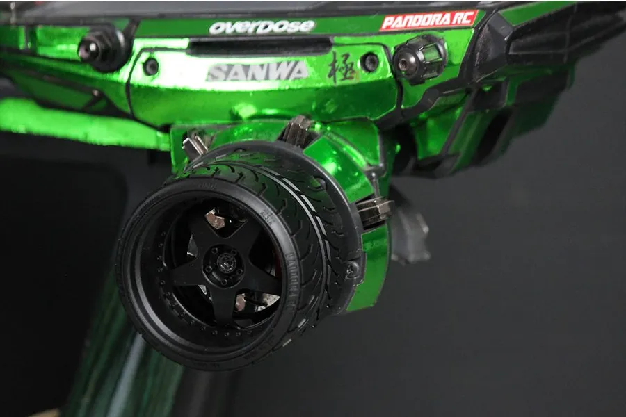 A close-up of a custom green metallic RC transmitter steering wheel accessory installed on a Sanwa radio controller.