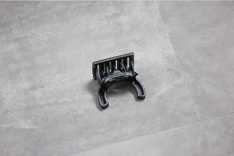 A black plastic Pandora RC steering wheel accessory for Sanwa transmitters, shown from an angled top-down perspective on a grey surface.