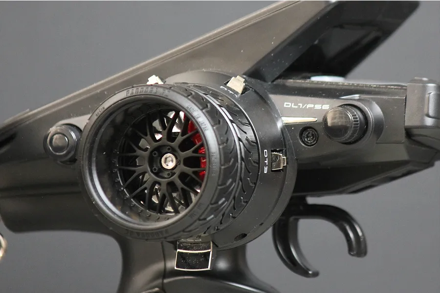 Close-up of a Pandora RC custom steering wheel accessory installed on a black RC transmitter, featuring a realistic wheel and tire design.