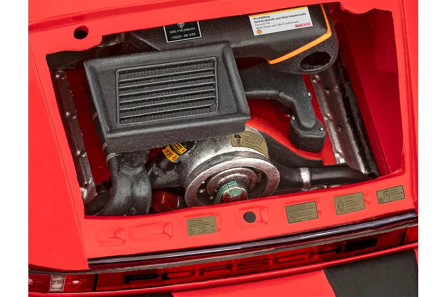 Close-up of the detailed engine bay of a 1/24 scale Revell Porsche 911 Turbo model kit, showing the engine block, intercooler, and various warning decals.