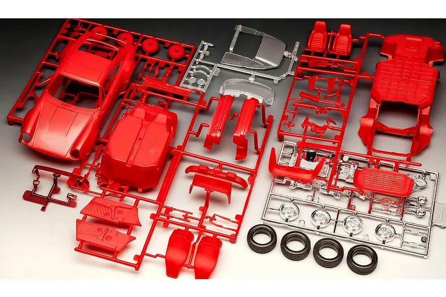 Plastic model kit parts for a 1975 Porsche 911 Turbo, including red car body, chassis, interior, chrome wheels, and black rubber tires on sprues.