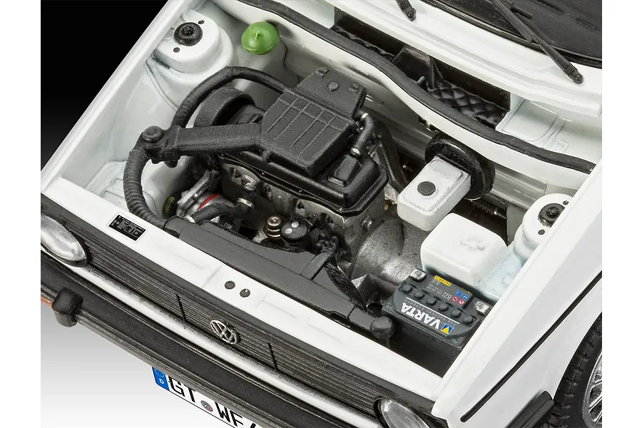 Close-up of the detailed engine bay of a 1/24 scale Revell 1974 VW Golf 1 model kit, showing the engine block, battery, and white body panels.