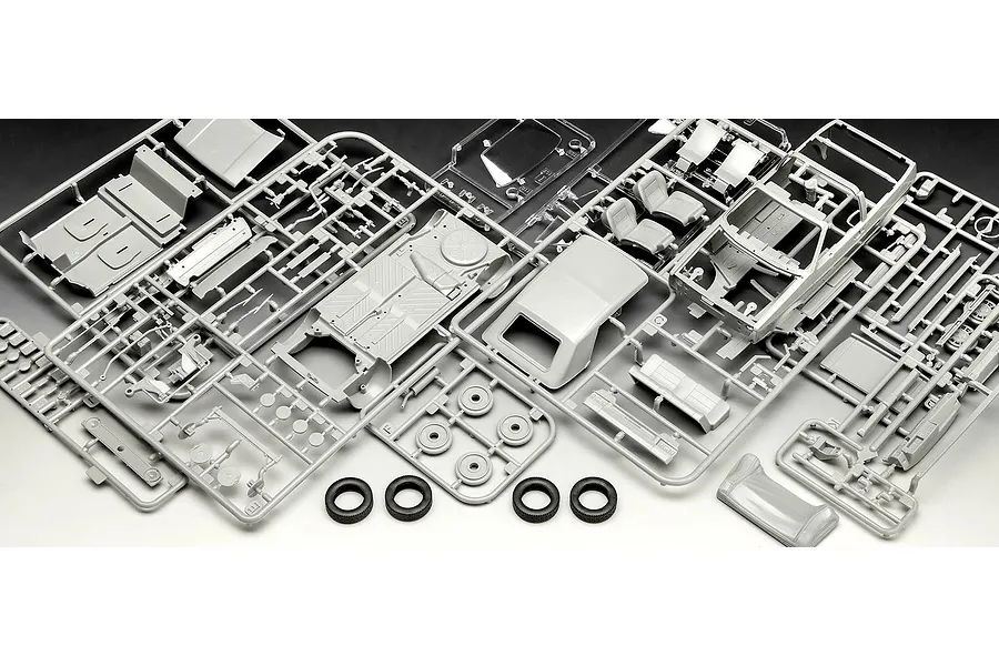 Unassembled plastic model kit parts for a 1/24 scale VW Golf 1, including grey sprues with car body, interior, and chassis components, plus four black rubber tires.