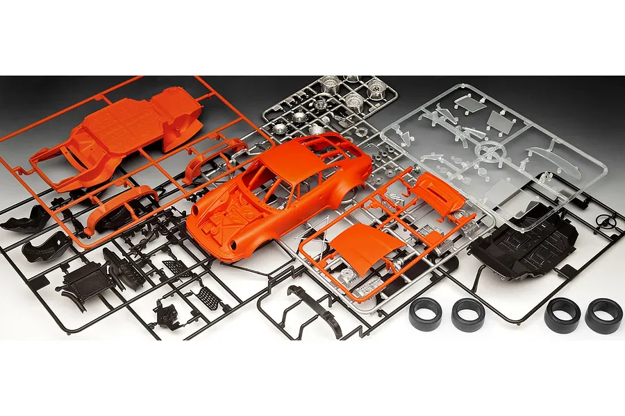 Plastic model kit parts for a Revell Porsche 934 RSR, including orange car body, black chassis, and clear windows on sprues.