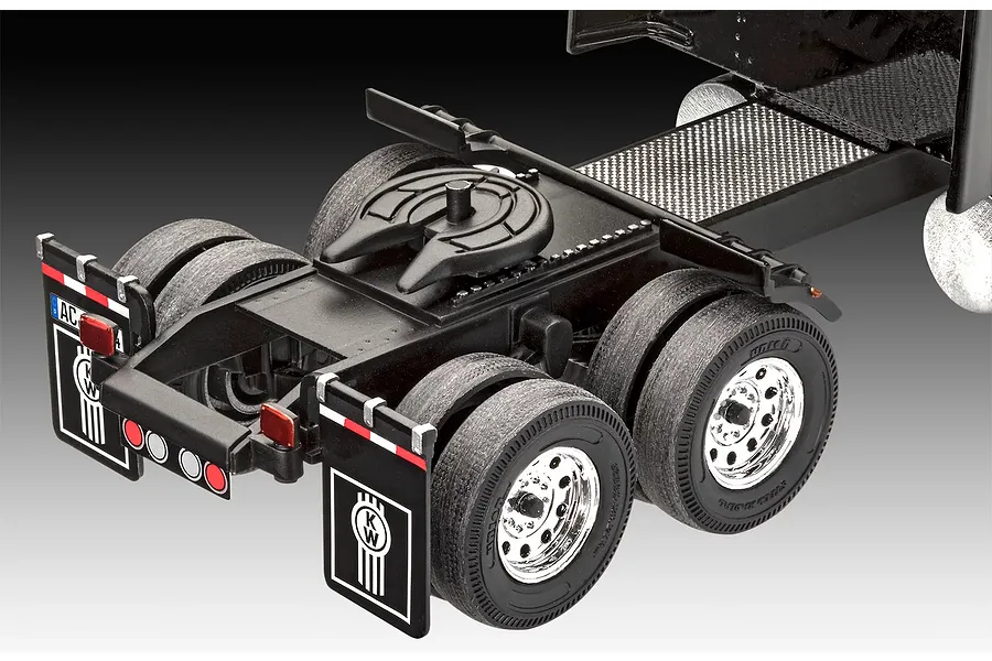 Close-up of the rear chassis and dual wheels of a Kenworth model truck, showing the fifth wheel hitch and mudflaps with the KW logo.