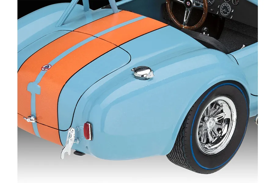 Close-up of the rear section of a light blue and orange Shelby Cobra 427 model car, showing the trunk, fuel cap, and rear wheel.