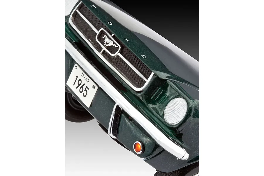 Close-up of the front grille and bumper of a dark green 1965 Ford Mustang model car, showing the Mustang emblem and Texas license plate.