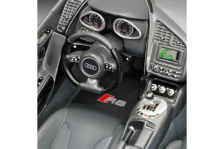 Close-up of the detailed interior of a 1/24 scale Revell Audi R8 plastic model car, showing the dashboard, steering wheel, and R8 branded floor mat.
