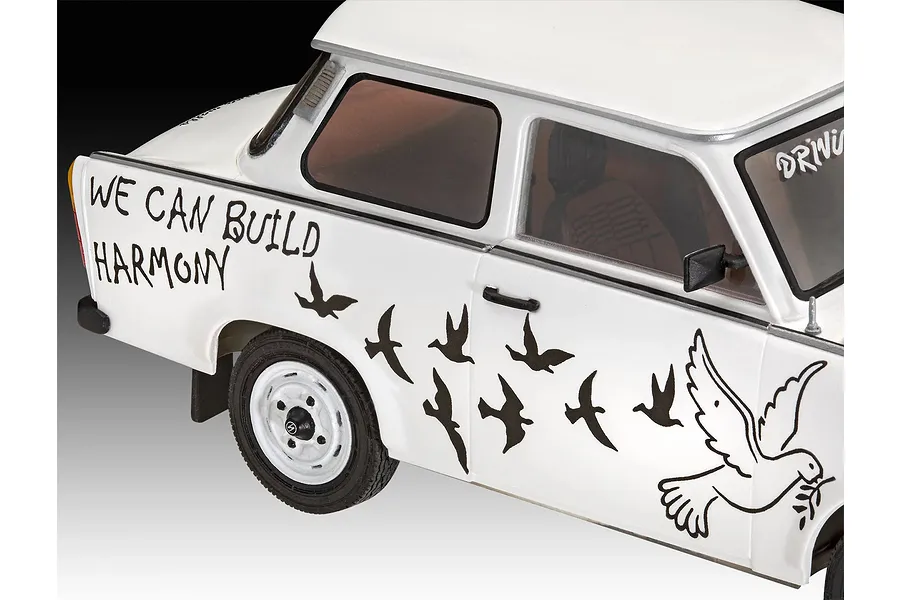 A close-up of a white 1/24 scale Trabant 601S model car featuring black decals of birds and the text WE CAN BUILD HARMONY on the side panel.