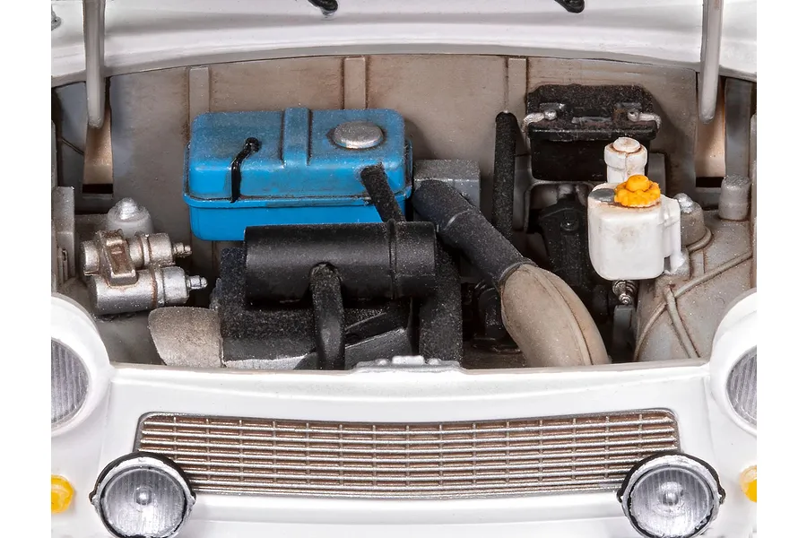 Close-up of the detailed engine bay of a 1/24 scale Trabant 601S model car, showing a blue fuel tank, black engine components, and white bodywork.