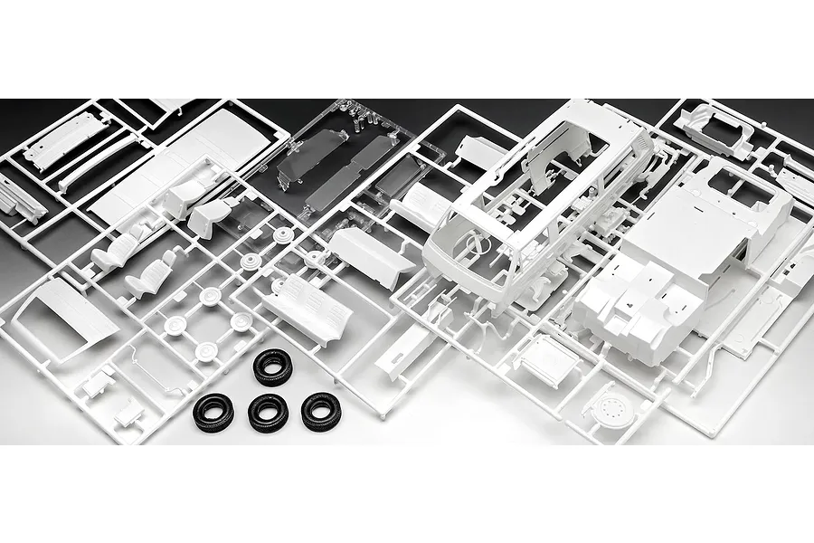 Unassembled white plastic model kit parts for a VW T3 bus on sprues with black rubber tires.