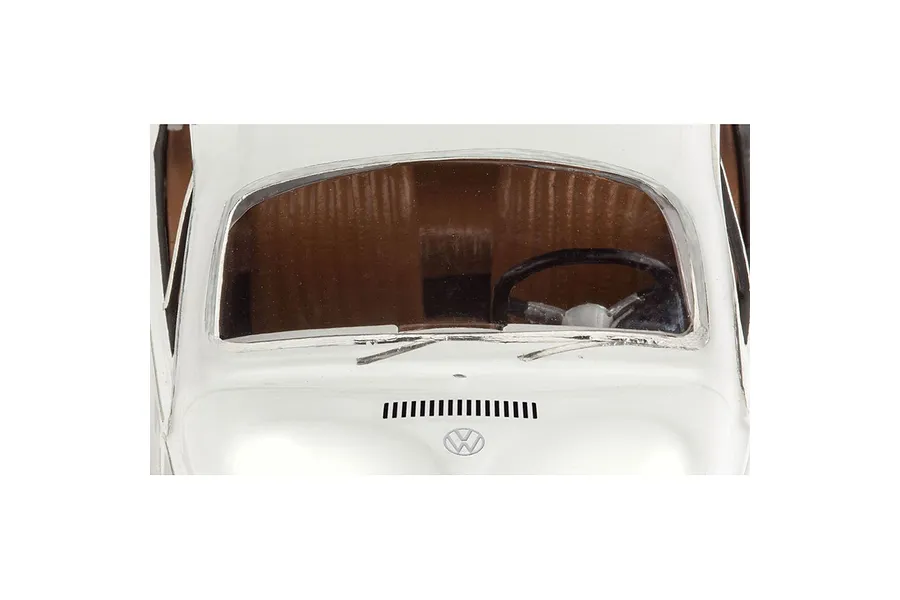 Close-up of the windshield and hood area of a white VW Beetle model car, showing the steering wheel, dashboard, and Volkswagen logo.