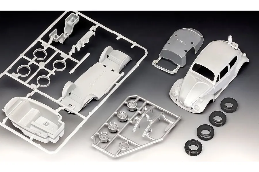 Unassembled plastic model kit parts for a 1/32 scale VW Beetle, including a car body, chassis sprue, wheel sprue, and four rubber tires.