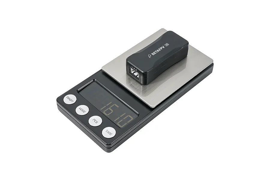 A black BetaFPV BT3.0 2S battery charger and voltage tester sitting on a digital weighing scale against a white background.