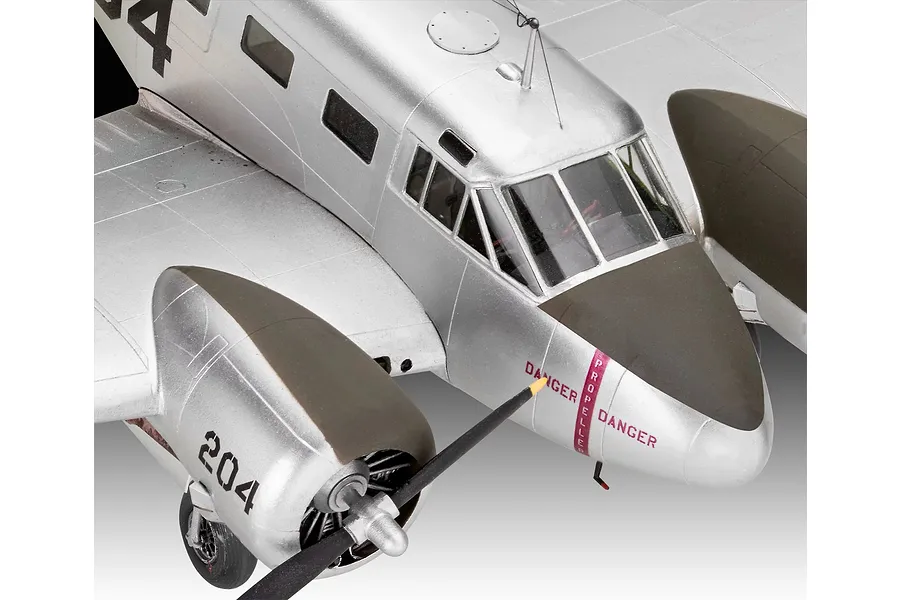 Close-up of a 1/48 scale Beechcraft Model 18 plastic model aircraft, showing the silver fuselage, cockpit windows, and engine cowling with propeller.