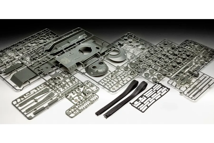 A collection of grey plastic model tank parts on sprues and two black rubber tank tracks laid out on a white surface.