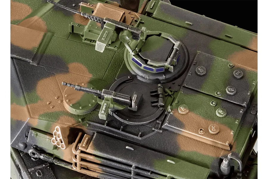 Top-down view of a 1/72 scale plastic model M1 Abrams tank turret featuring detailed camouflage paint, hatches, and mounted machine guns.