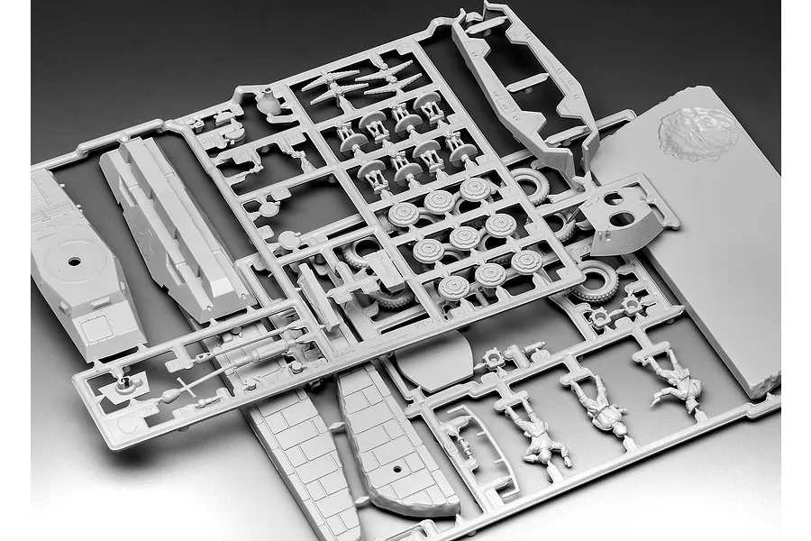A grey plastic sprue containing various unpainted model parts for a military vehicle and figures, including wheels, hull sections, and soldier figurines.