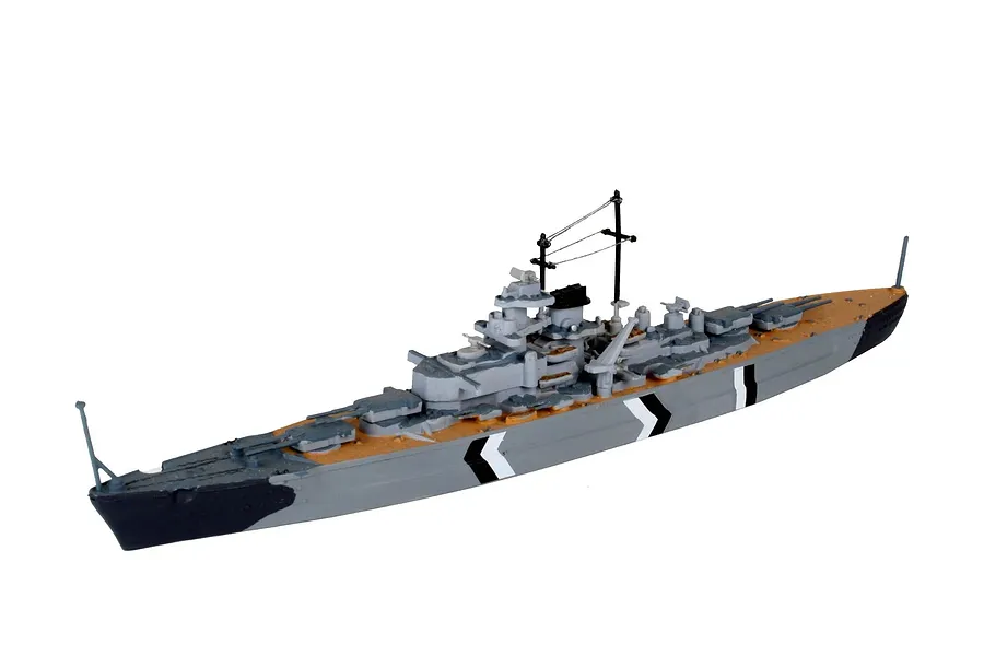 A 1/1200 scale plastic model of the German battleship Bismarck, featuring grey hull, tan deck, and black and white camouflage markings.