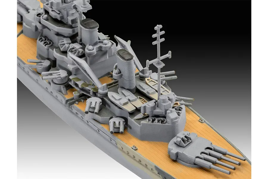 A high-angle close-up of a 1/1200 scale plastic model battleship, showing the grey superstructure, tan deck, and gun turrets.