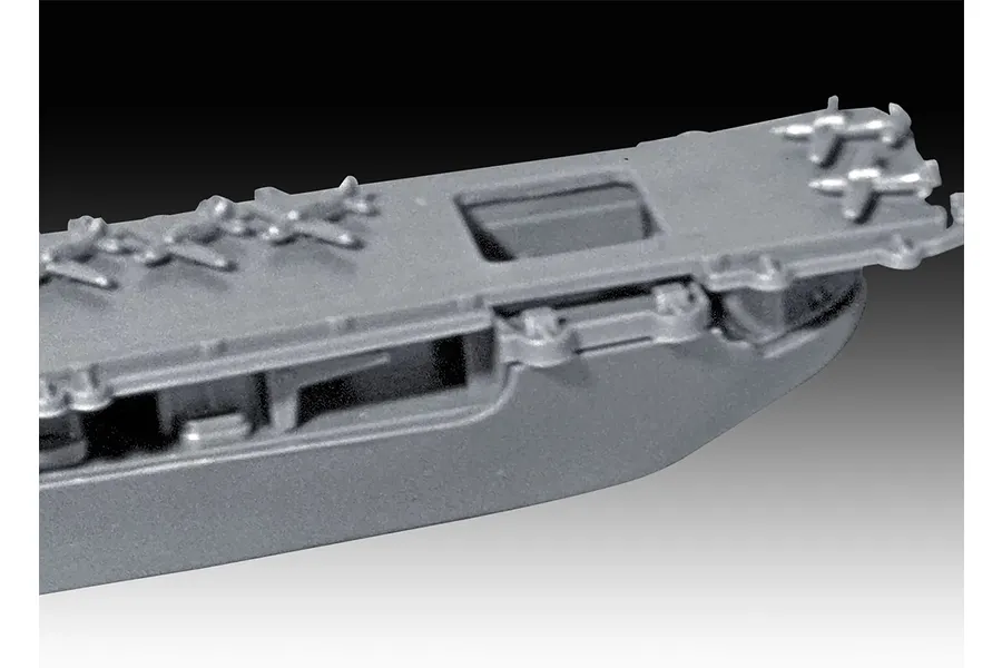 Close-up of a grey plastic model aircraft carrier deck with molded miniature planes, showing the bow section.