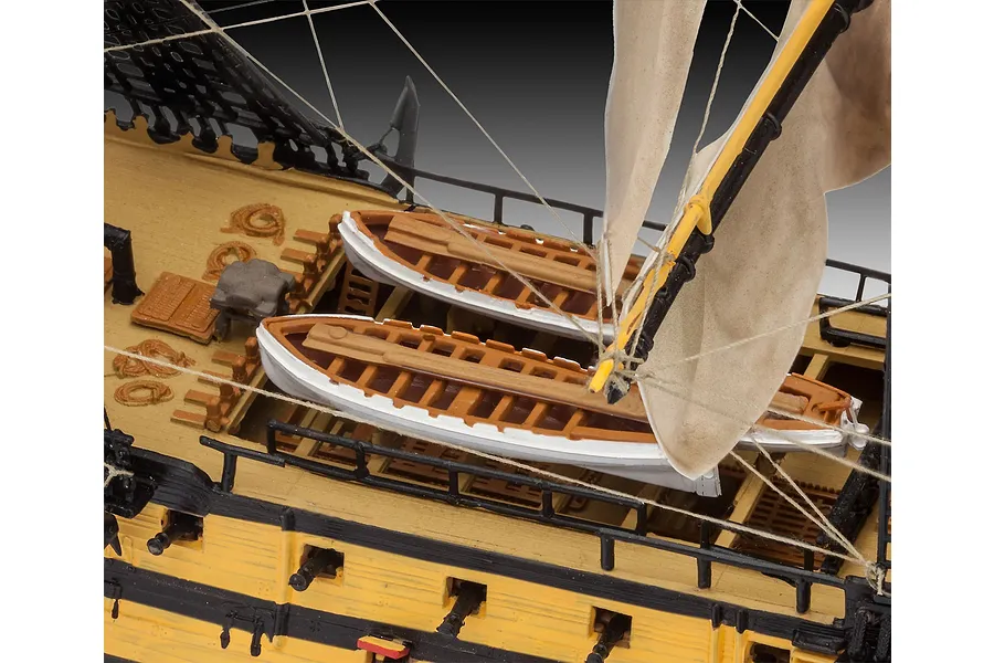 Close-up of the deck of a Revell HMS Victory model ship, showing two small lifeboats, rigging, and masts against a grey background.