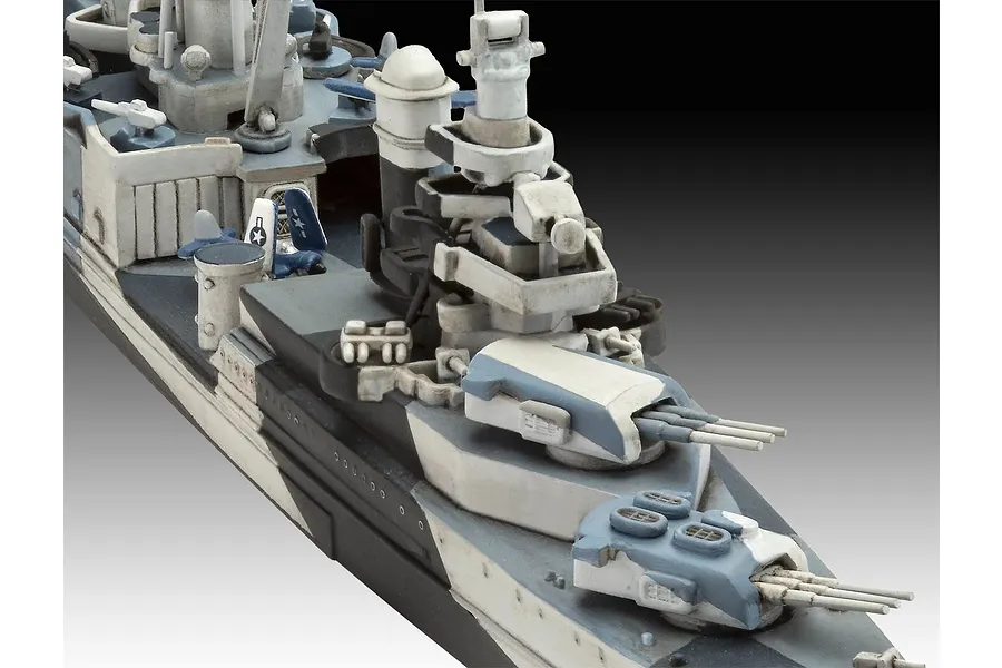 Close-up of a painted 1/700 scale plastic model warship showing the forward deck, gun turrets, and bridge structure with a blue and white camouflage pattern.