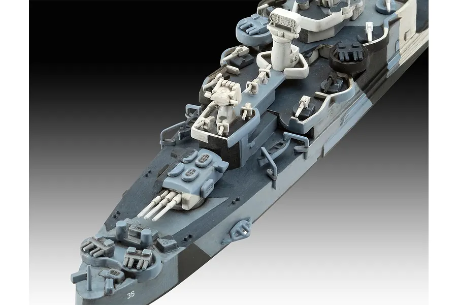 A high-angle close-up view of a 1/700 scale plastic model ship, showing the deck details, gun turrets, and camouflage paint scheme.