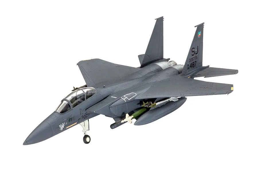 A completed 1/144 scale plastic model of an F-15E Strike Eagle fighter jet in dark grey, featuring external fuel tanks and missiles.
