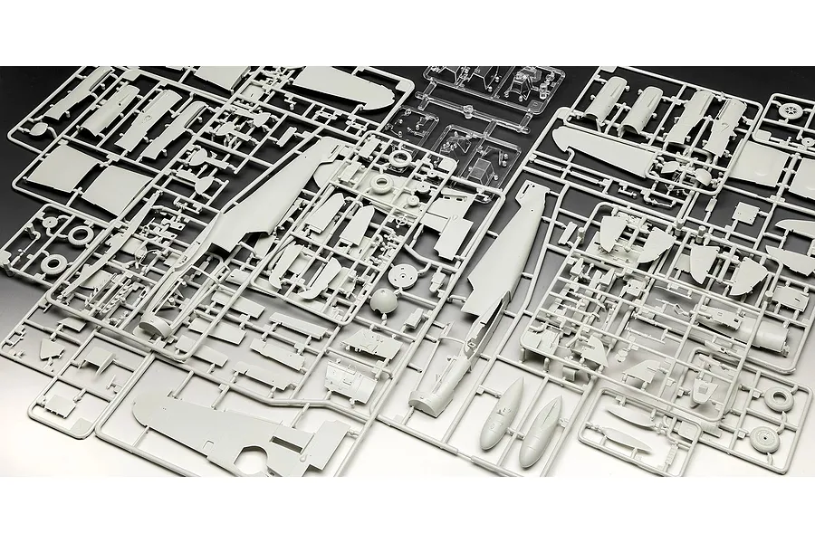 Several grey plastic model kit sprues containing various aircraft parts for a Messerschmitt Bf 109 model, including fuselage and wing sections.