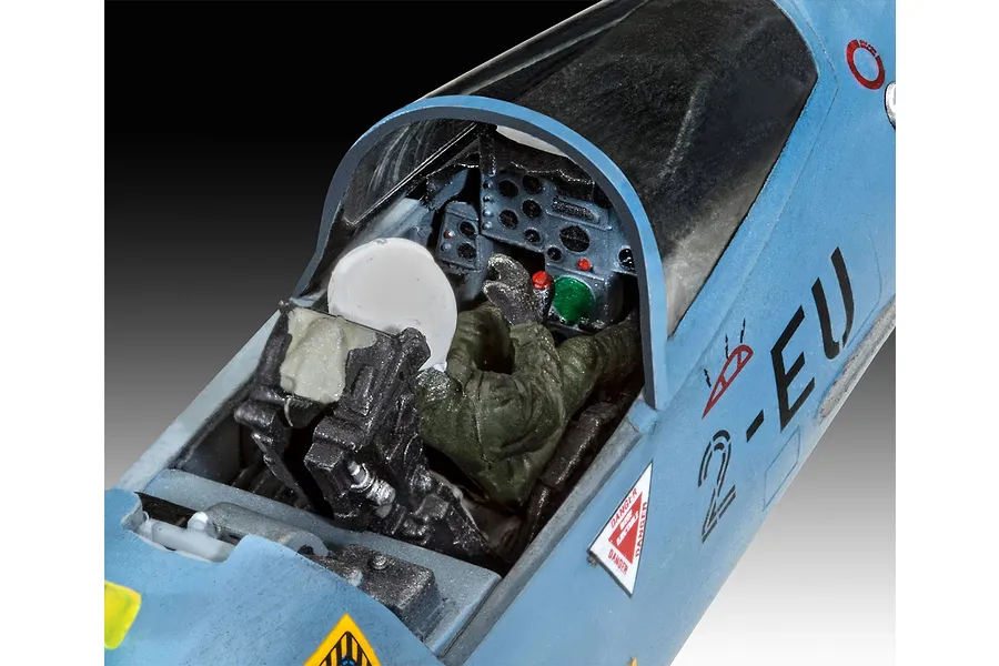 Close-up of a painted plastic model aircraft cockpit with a pilot figure seated inside, showing instrument panel details and fuselage markings.