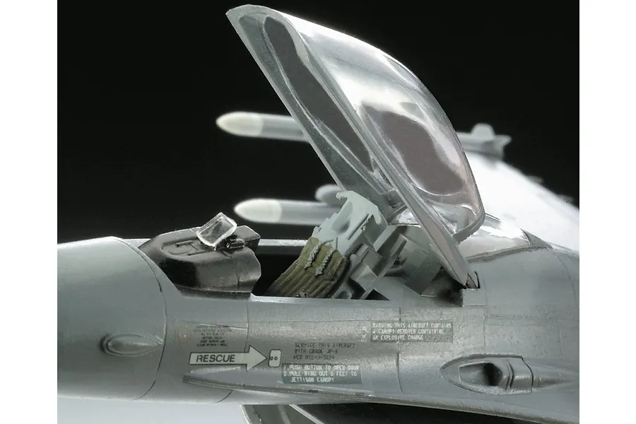 Close-up of a plastic model F-16 fighter jet cockpit with the canopy open, showing detailed decals and ejection seat.