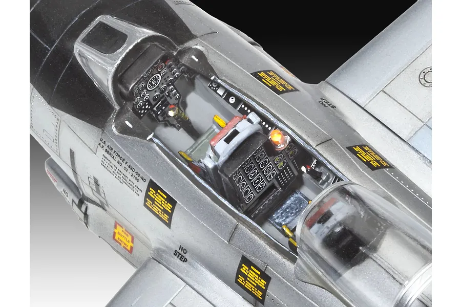 Close-up of a detailed plastic model aircraft cockpit showing instrument panels, seat, and decals on a silver fuselage.