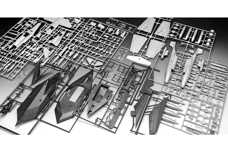 Multiple plastic model kit sprues containing parts for aircraft models, including grey and black components laid out on a flat surface.