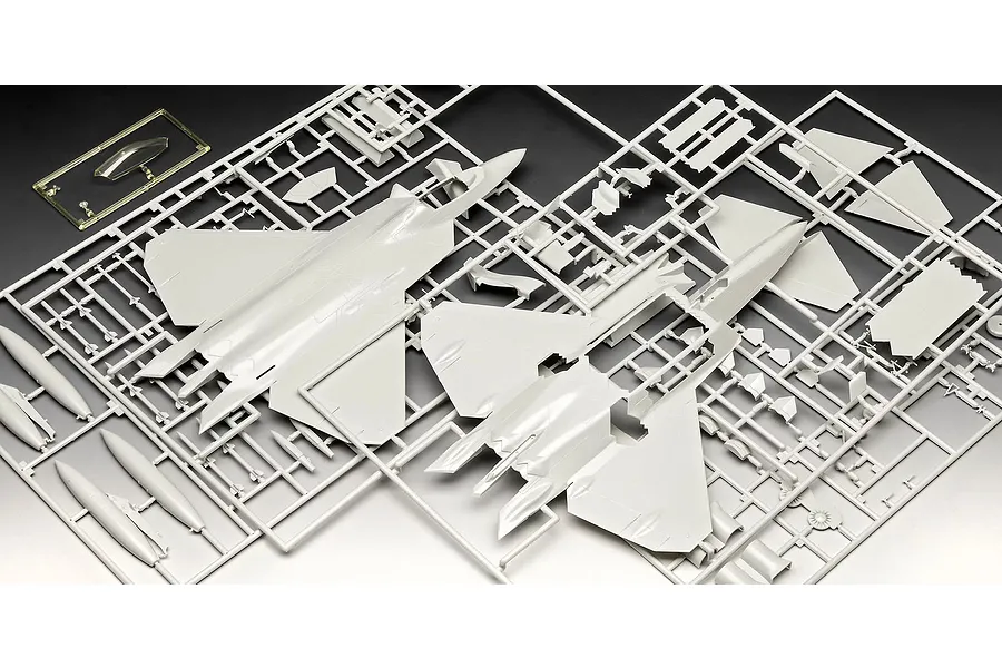Plastic model kit sprues for a 1/72 scale F-22A Raptor aircraft, showing grey fuselage parts and a clear canopy piece on a dark background.
