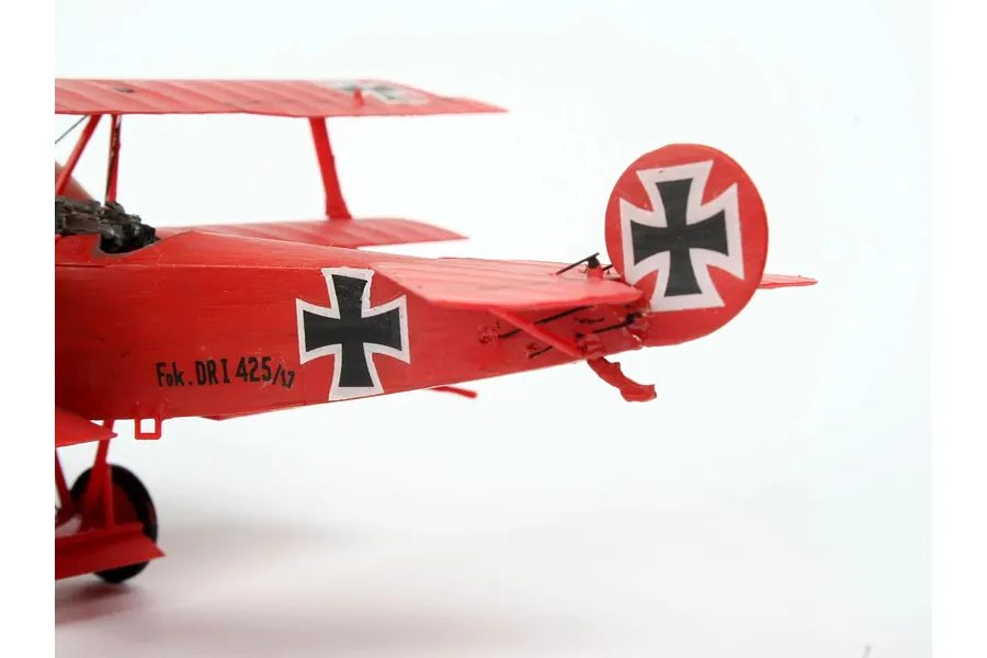A close-up side view of a red Fokker DR.1 triplane plastic model kit showing the tail section with German cross markings.