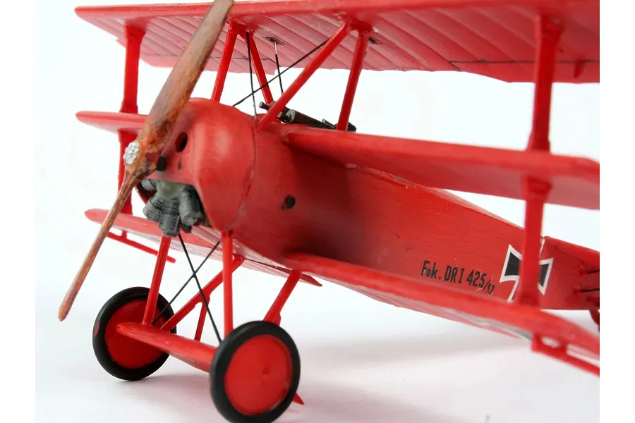 A close-up, side-angle view of a red Fokker DR.1 triplane plastic model aircraft on a white background.