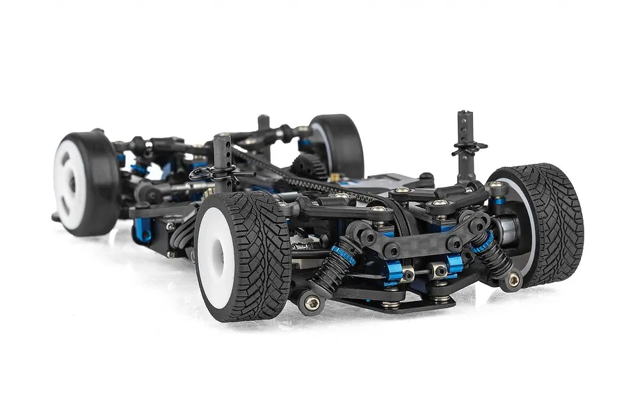 A low-angle studio shot of a Team Associated TC28 1/28 scale RC touring car chassis showing the front suspension, blue anodized components, and treaded tires.