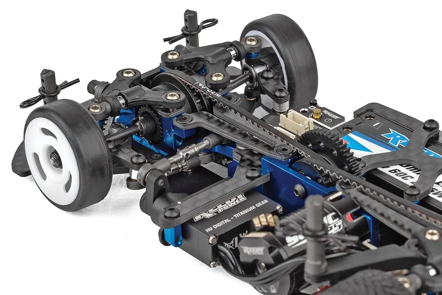 Close-up of the front chassis assembly of a Team Associated RC touring car, showing blue anodized aluminum, black plastic parts, and a belt drive system.
