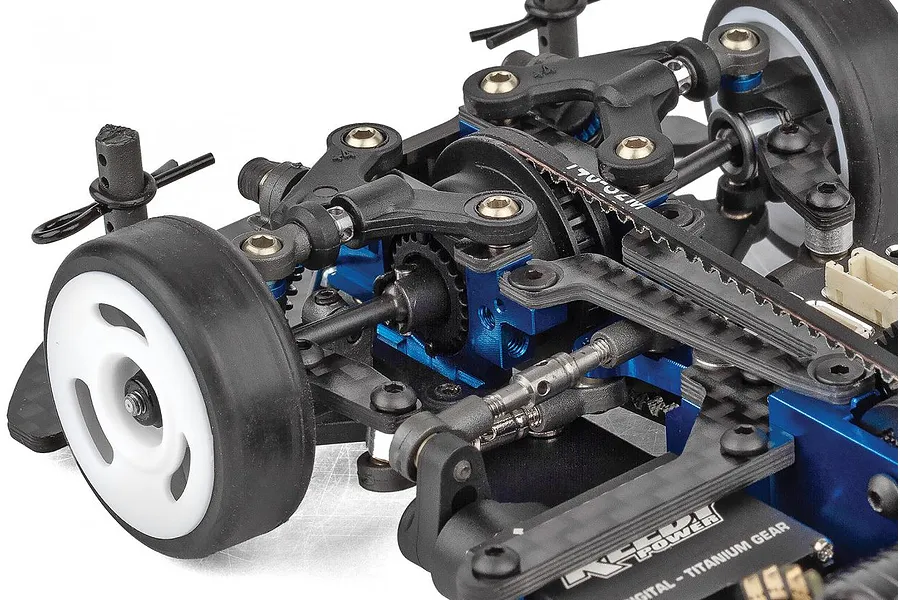 Close-up of the chassis and suspension components of a Team Associated RC car, showing blue anodized aluminum parts, a drive belt, and rubber tires.