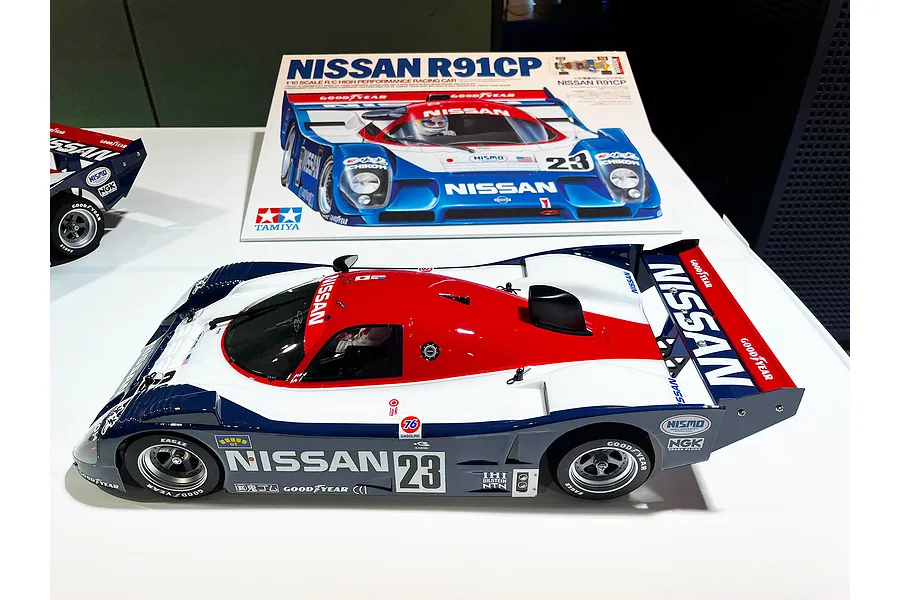 A Tamiya Nissan R91CP 1/10 scale RC car kit box and a fully assembled model car on a white surface.