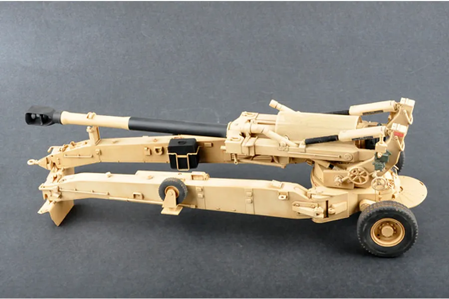 A 1/16 scale plastic model of an M198 155mm towed howitzer, painted in a desert tan camouflage scheme against a dark grey background.