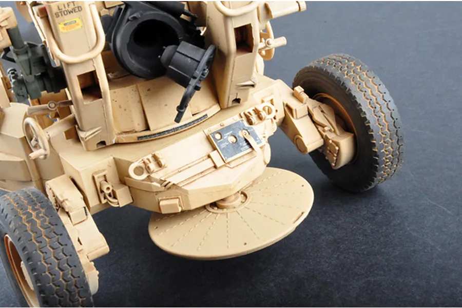 Close-up of a 1/16 scale M198 155mm towed howitzer model kit showing the firing platform, wheels, and tan chassis details.
