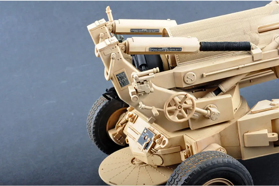 Close-up of a 1/16 scale M198 155mm towed howitzer plastic model kit, showing detailed tan components, wheels, and mechanical controls.