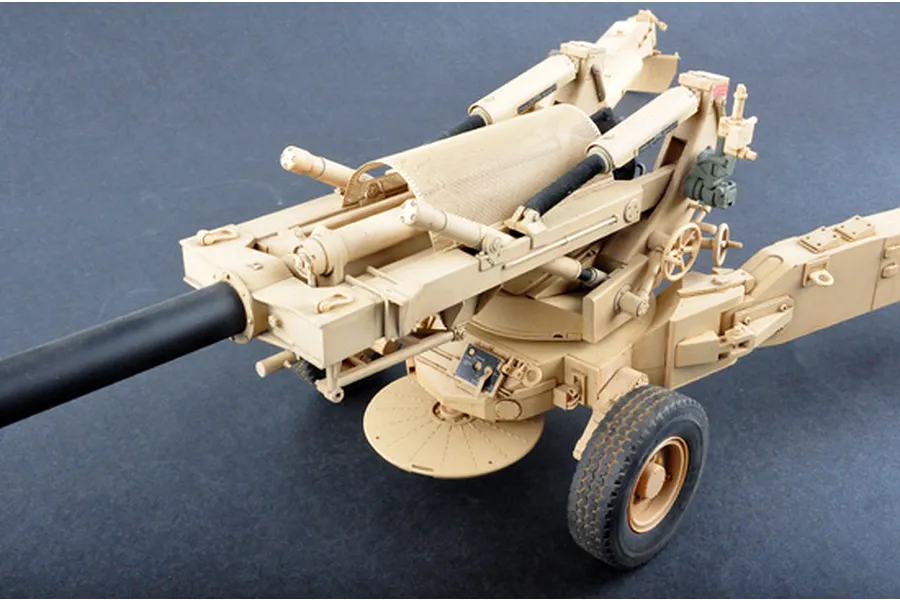 A high-angle studio shot of a 1/16 scale M198 155mm towed howitzer plastic model kit, painted in a desert tan camouflage scheme.