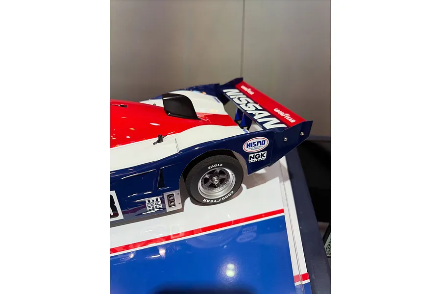 Close-up of the rear section of a Tamiya R91CP RC car model featuring Nissan livery, Goodyear tires, and Nismo branding on a display base.