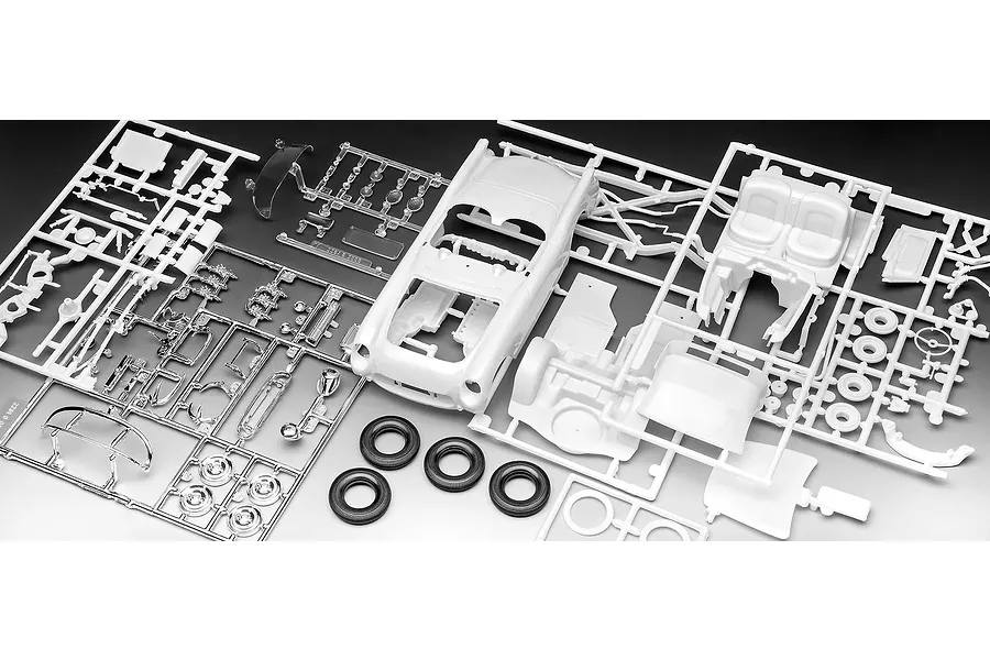 A collection of unpainted white plastic model car parts on sprues, including a car body, interior, and chrome-plated parts, with three black rubber tires.