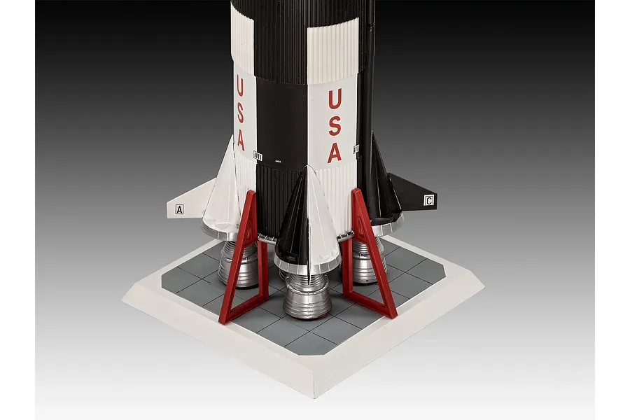 Close-up of the base of a Revell 1/96 scale Saturn V rocket model, showing the engines, red support struts, and a square display base.