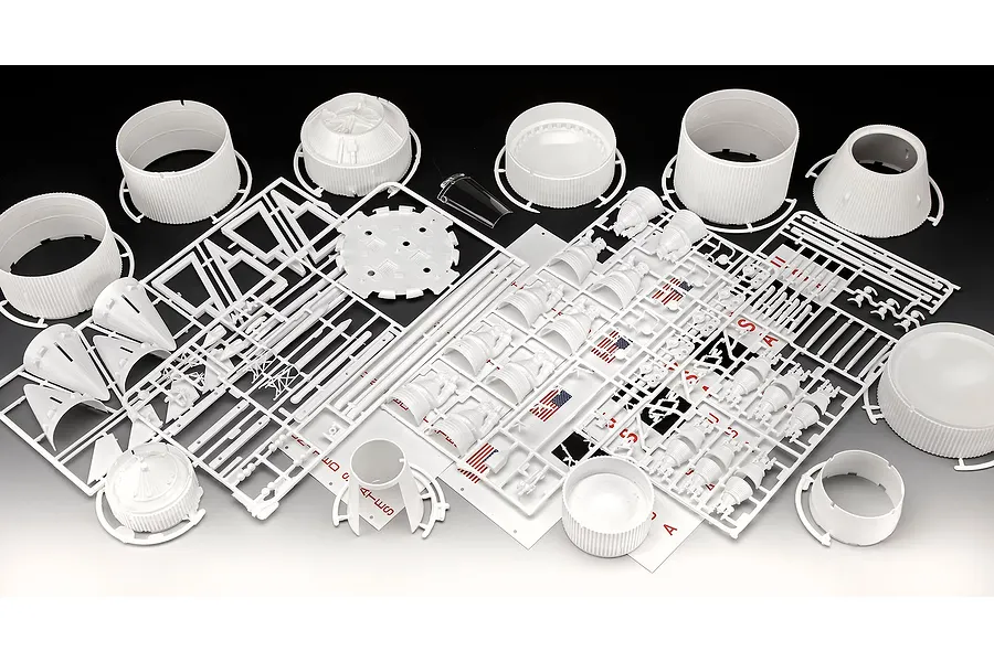 Unassembled plastic model kit parts for a Revell Saturn V rocket, including white cylindrical sections, engine nozzles, and decal sheets.